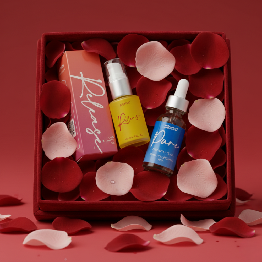 A red gift box holds CBD oil products nestled in a bed of red and pink rose petals.