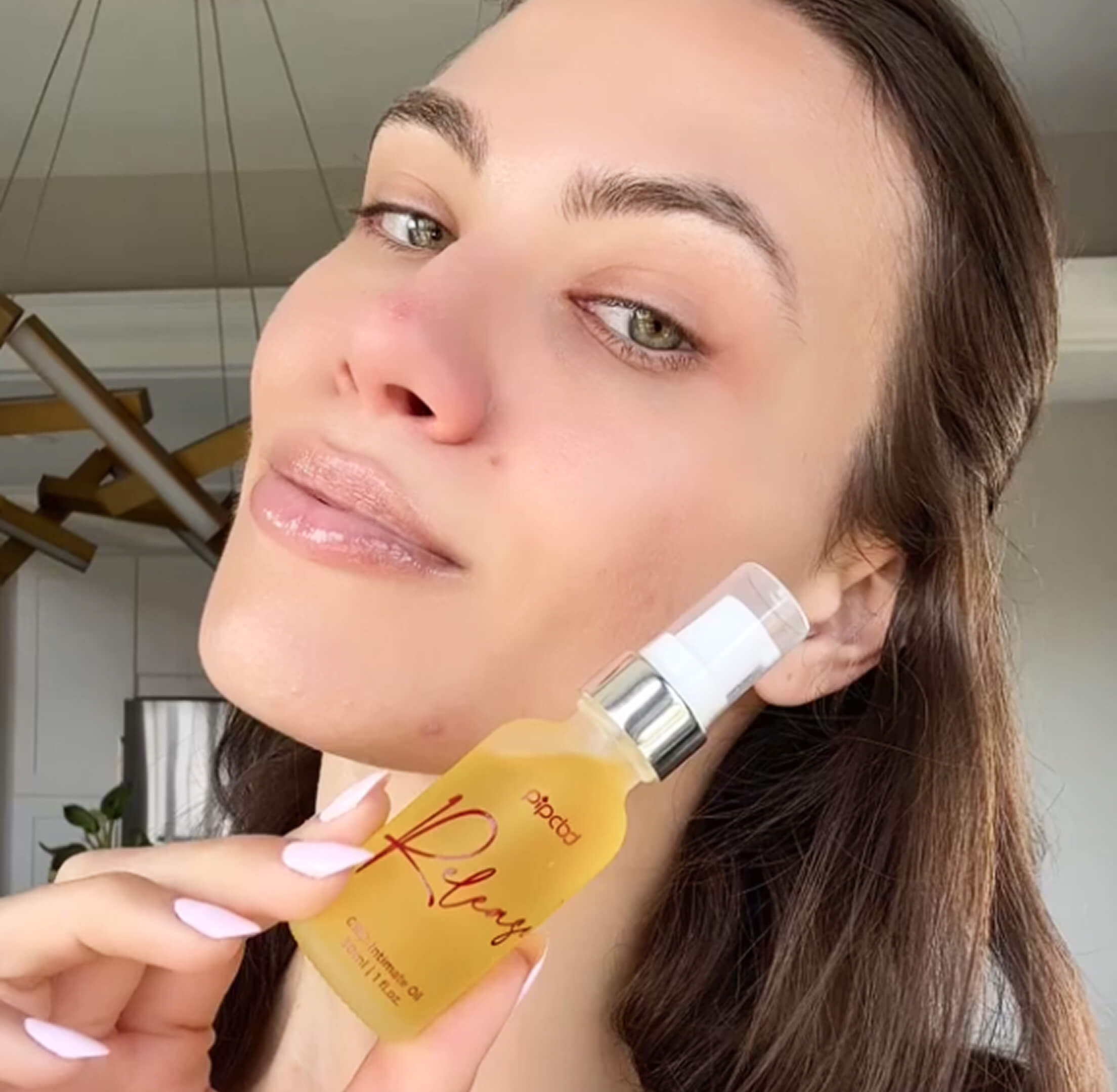 Person holding a bottle of skincare oil near their face.