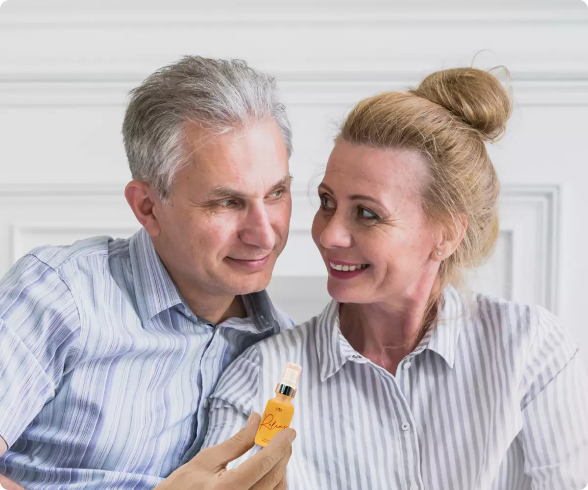 An older man and woman smile at each other while the man holds a small orange bottle.