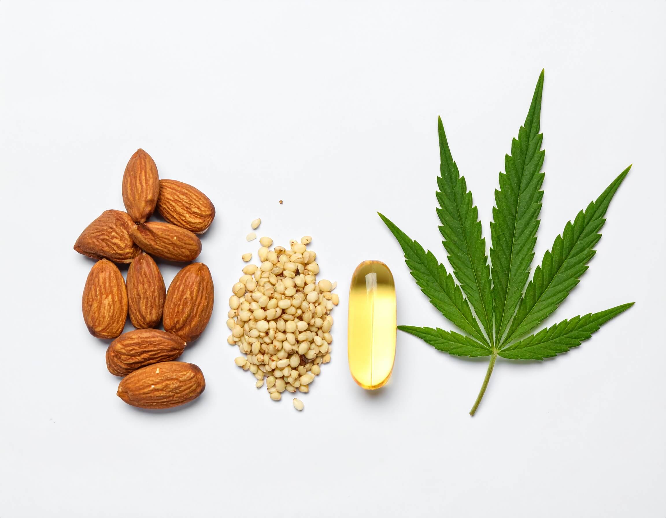 Almonds, seeds, oil capsule, and green leaf on white background.