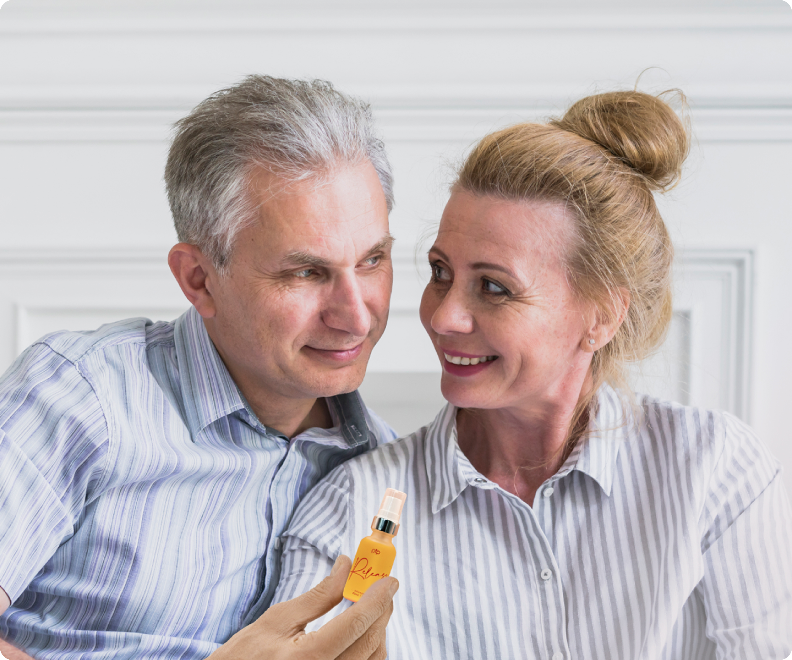 Smiling couple holding a small bottle, sitting together indoors.