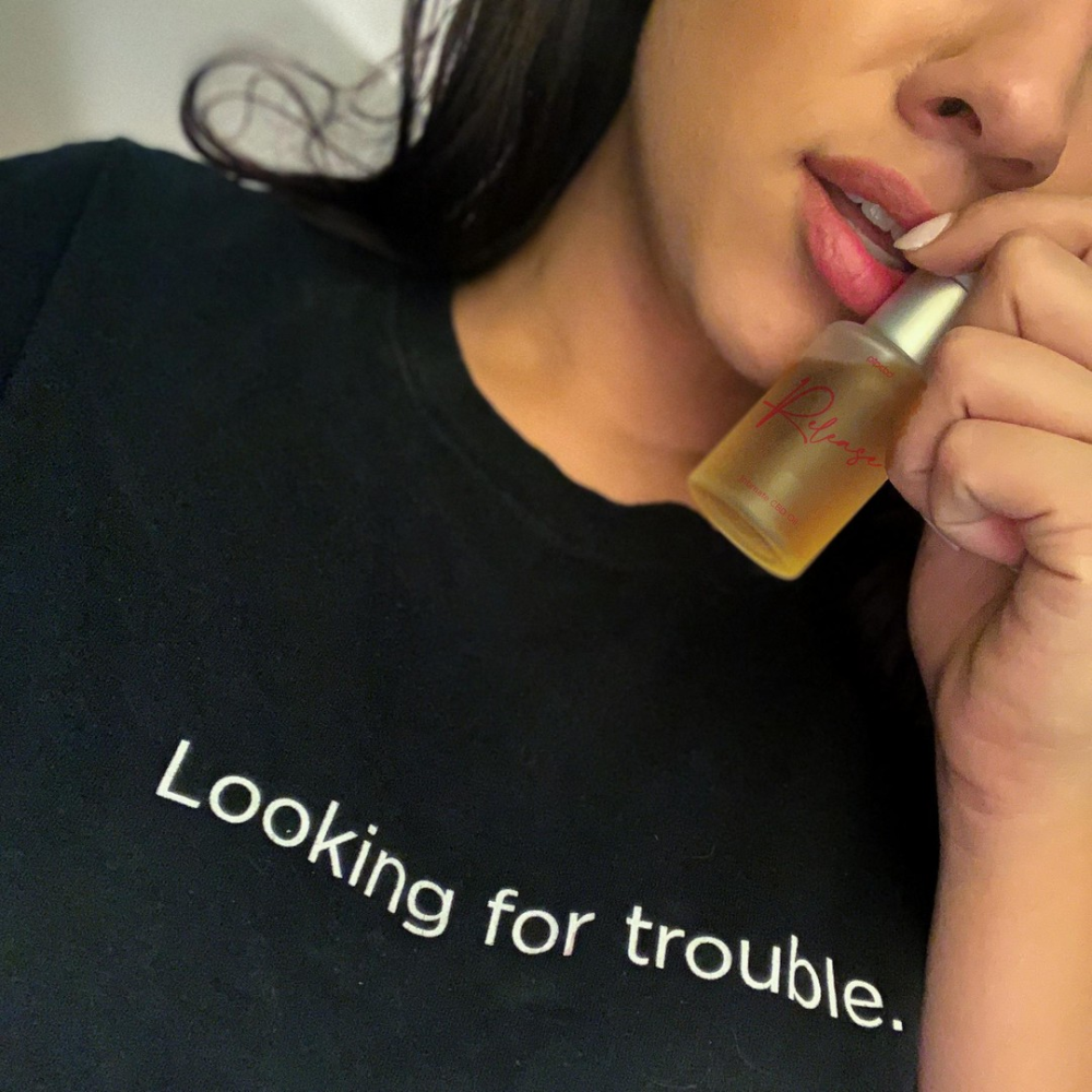 A person in a black t-shirt reading 'Looking for trouble' holds a small bottle near their mouth.