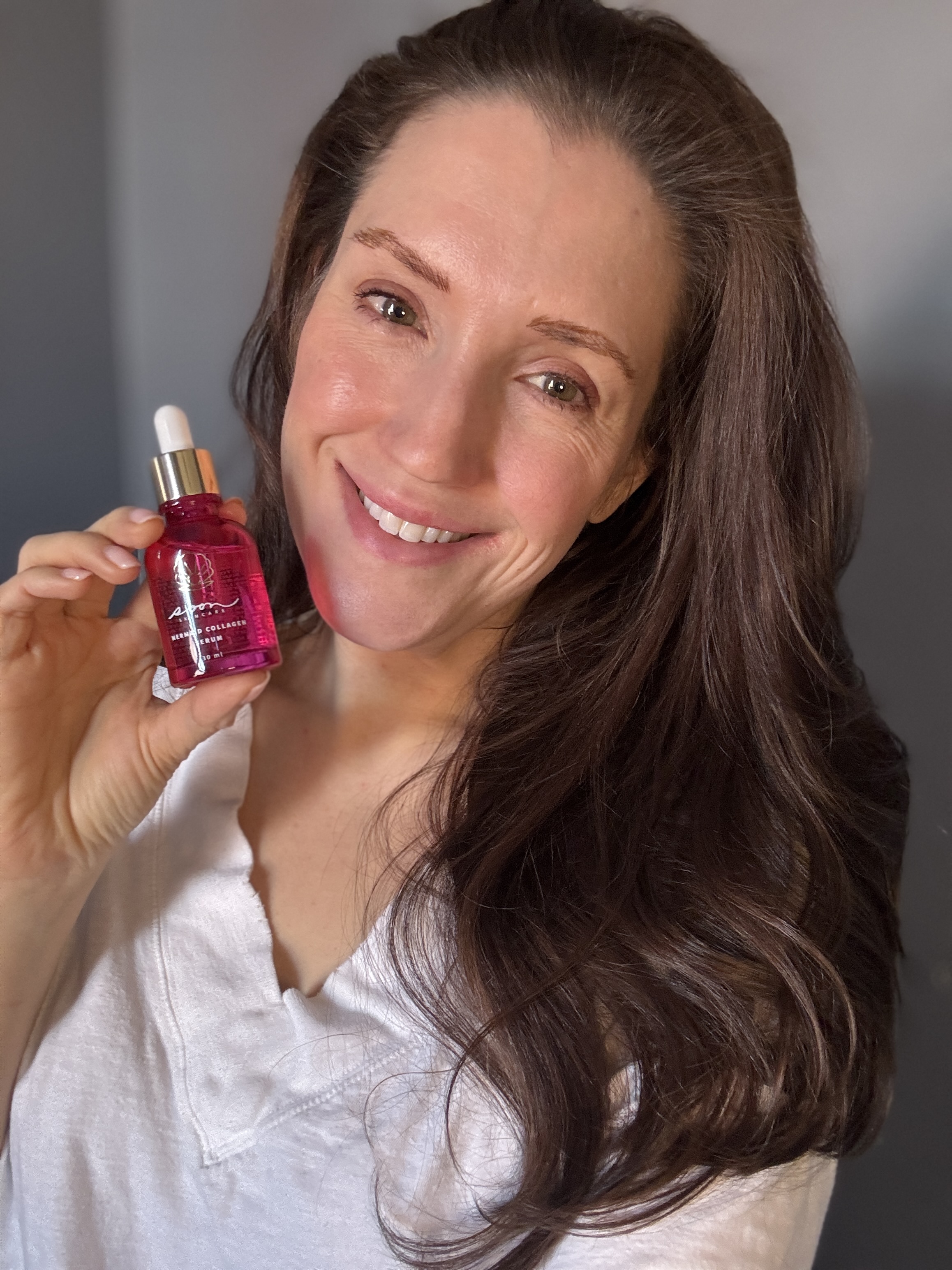 A person holding a pink skincare serum, smiling.