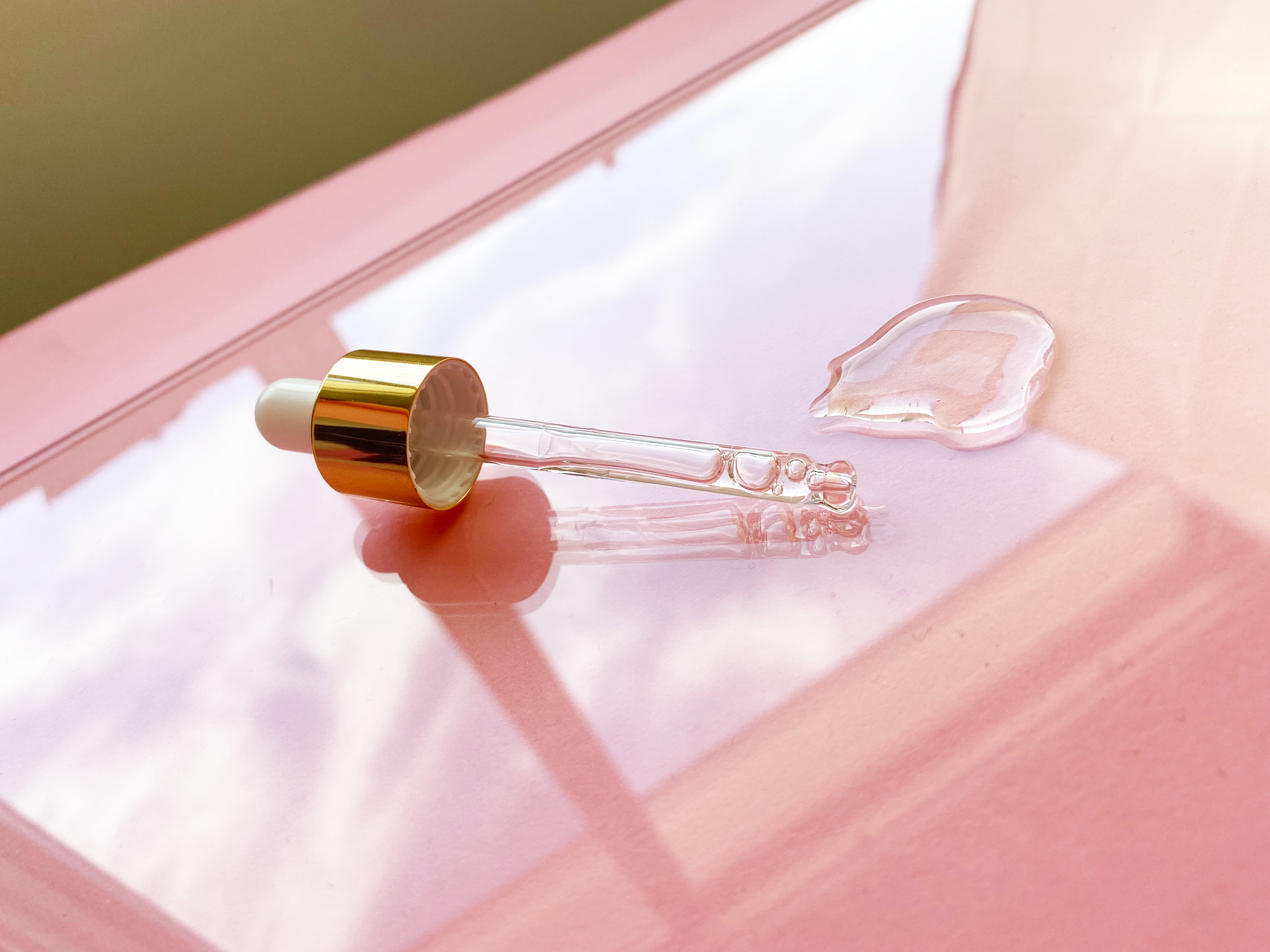 A dropper with liquid on a glossy, reflective pink surface.