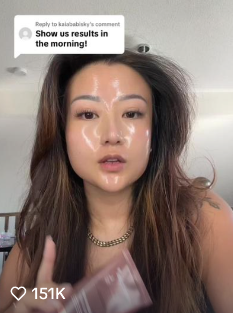 Person with shiny face holding a cosmetic tube indoors.