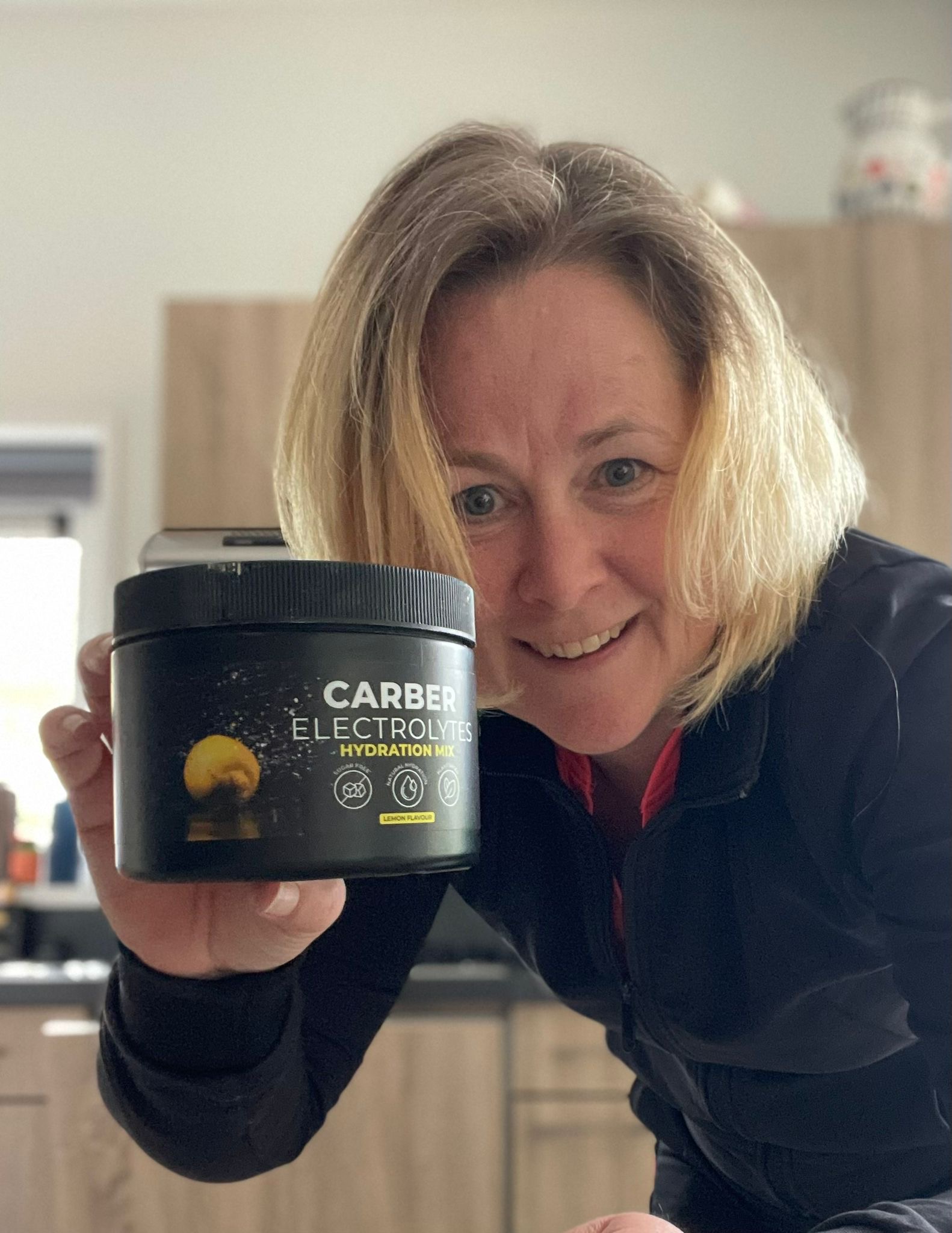 Person holding a container of Carber Electrolytes Hydration Mix in a kitchen.