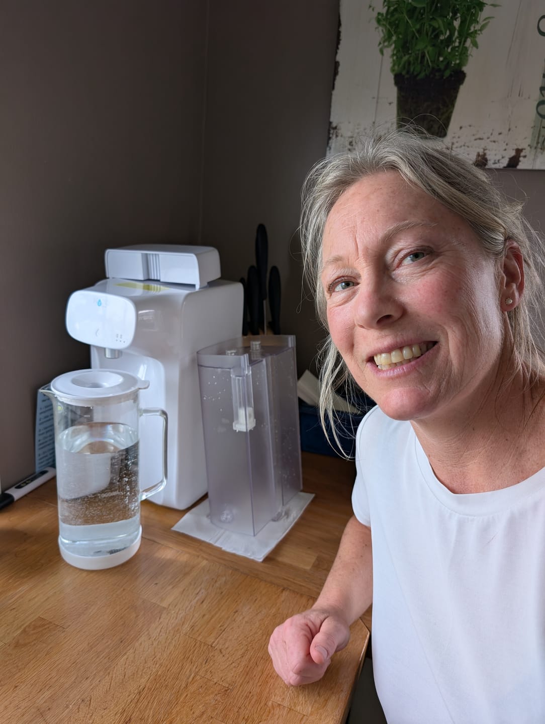 Woman smiling next to a water filtration machine on a wooden counter.