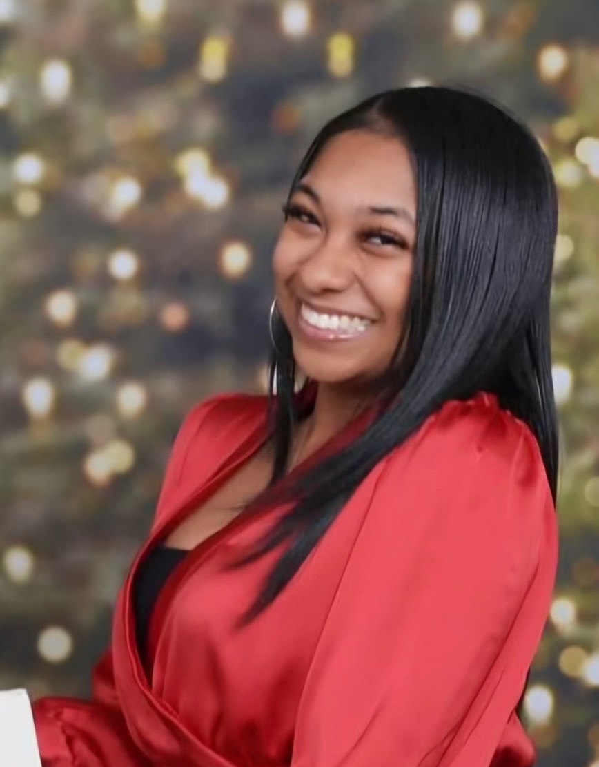Smiling woman in a red dress with a blurred festive background.