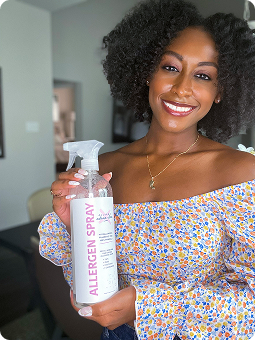 Person holding a bottle of allergen spray, smiling indoors.