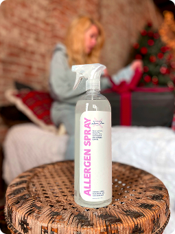 Allergen spray bottle on a wicker table, with a person and Christmas tree in the background.