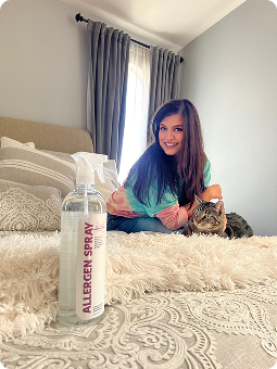 Woman sitting on bed with a cat, allergen spray bottle in foreground.