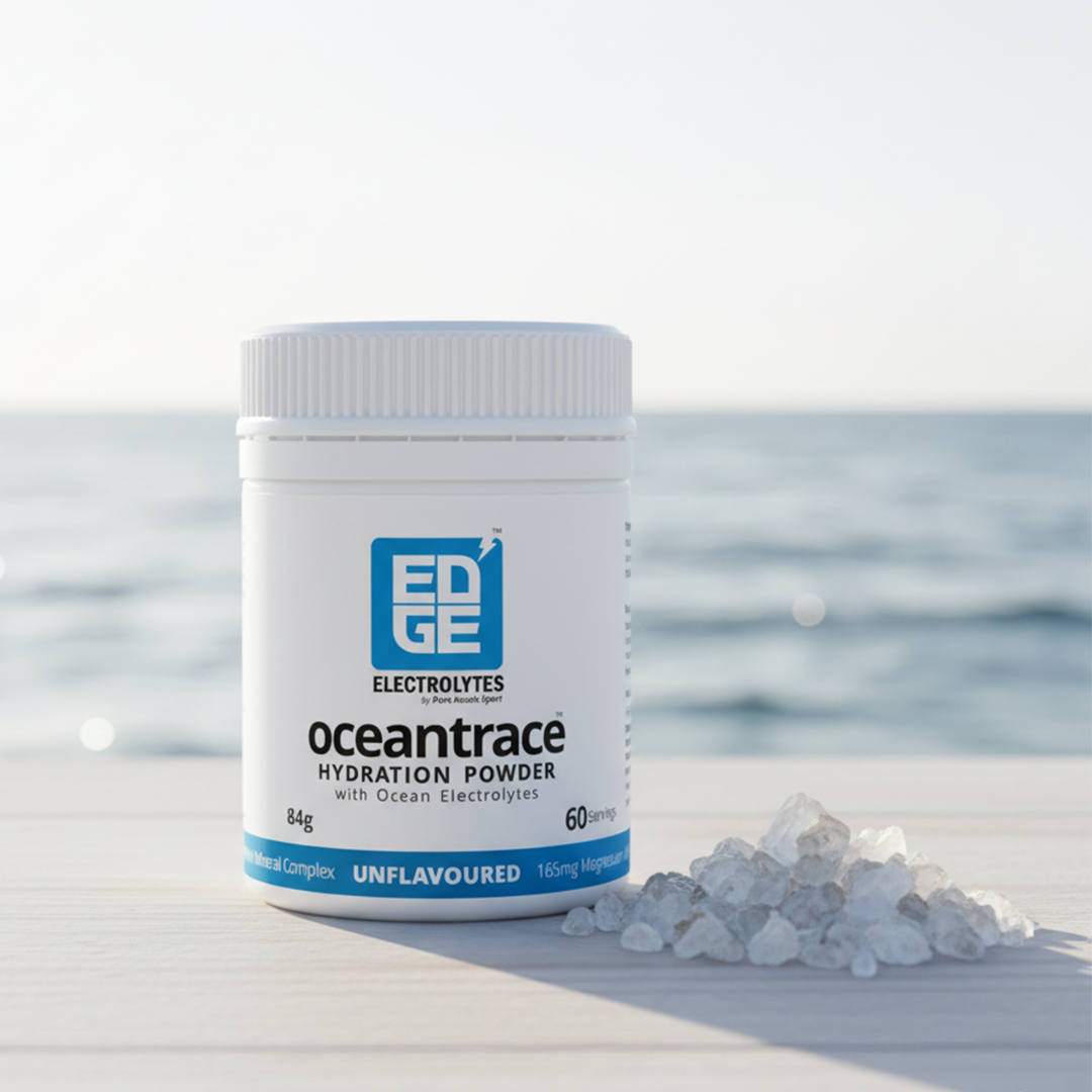 Ocean Trace hydration powder tub on a light wooden surface with ocean waves in the background and a small pile of mineral crystals beside it.
