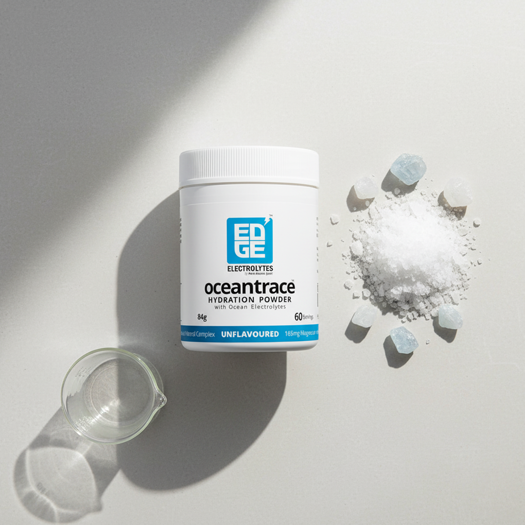 Flatlay of Ocean Trace hydration powder tub on a light surface, surrounded by a small glass beaker, a mound of white sea salt, and scattered blue mineral crystals.