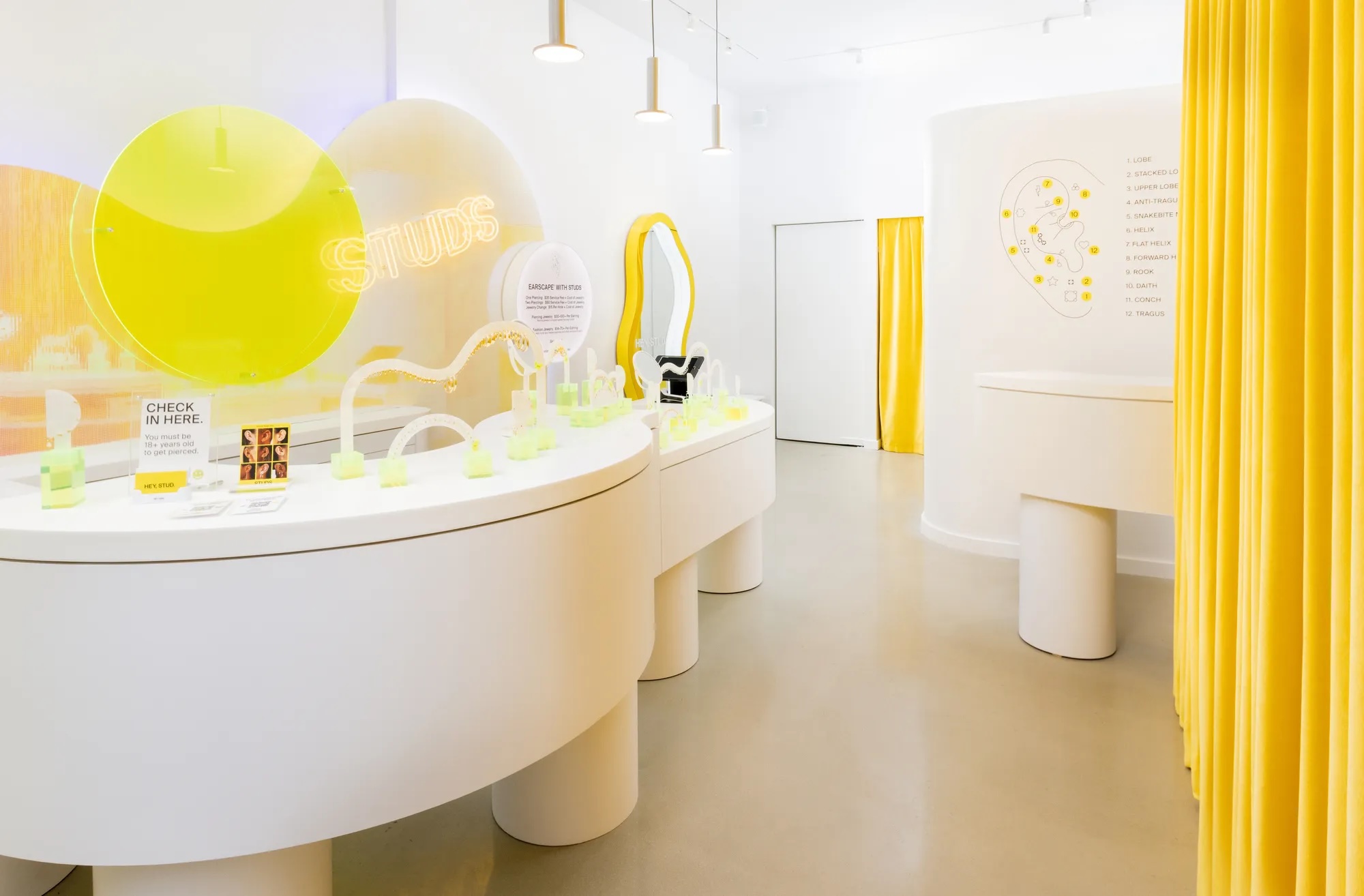 The bright, modern interior of a Studs piercing store, featuring white counters and vibrant yellow accents.