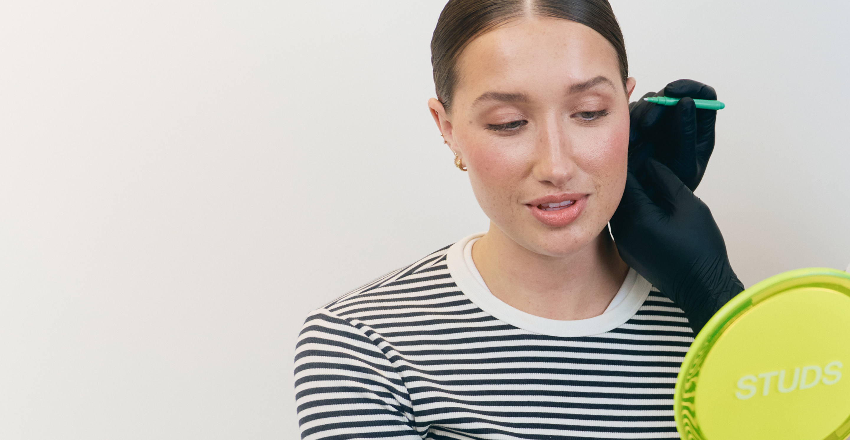 Person holding a hand mirror getting an ear piercing consultation.