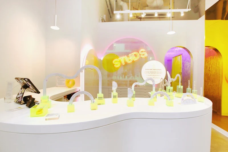 The brightly lit interior of a Studs store with a white counter displaying jewelry under a neon sign.