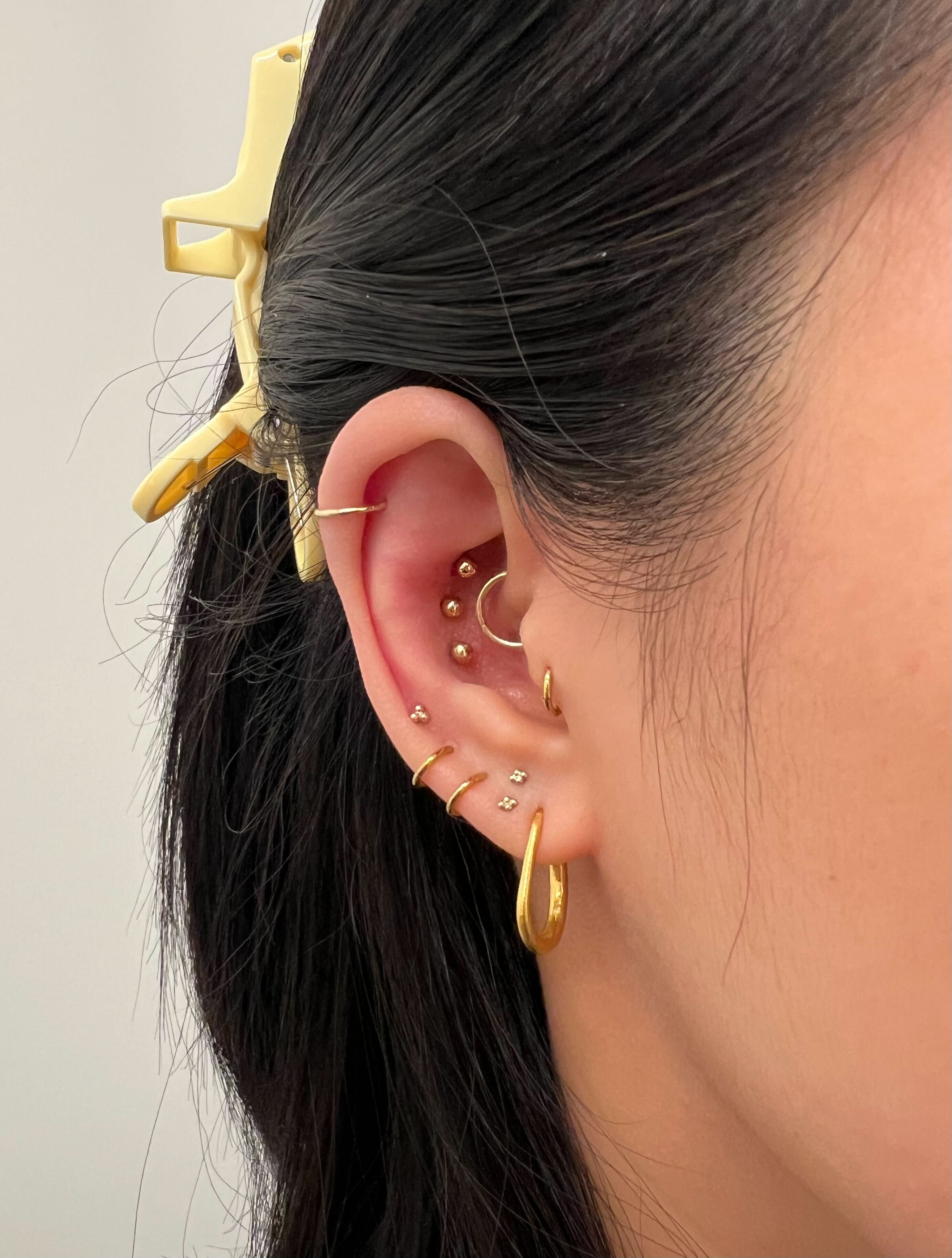 A close-up of a person's ear with numerous gold piercings and dark hair held by a clip.