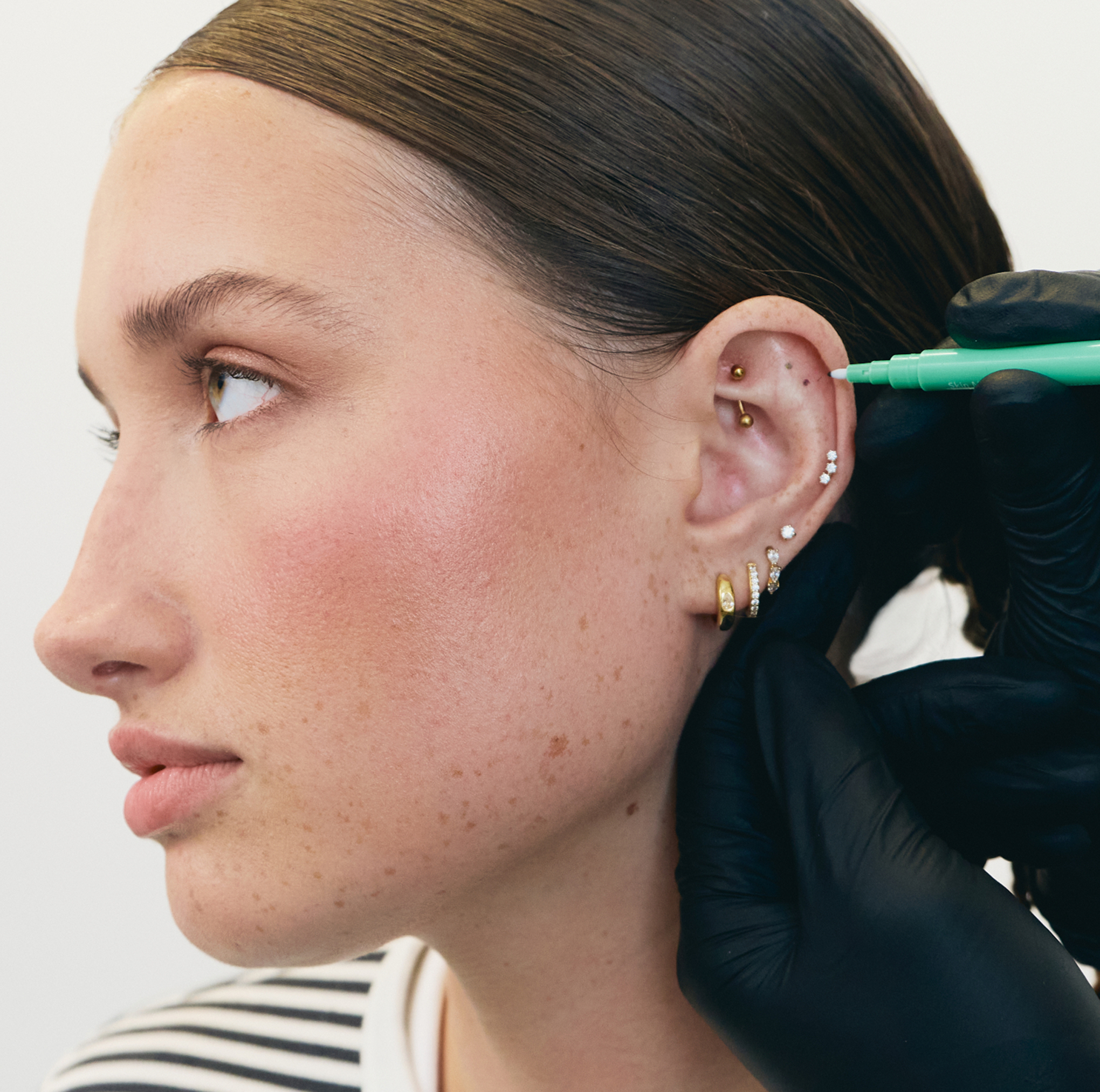 Person getting an ear piercing consultation, wearing a striped shirt.