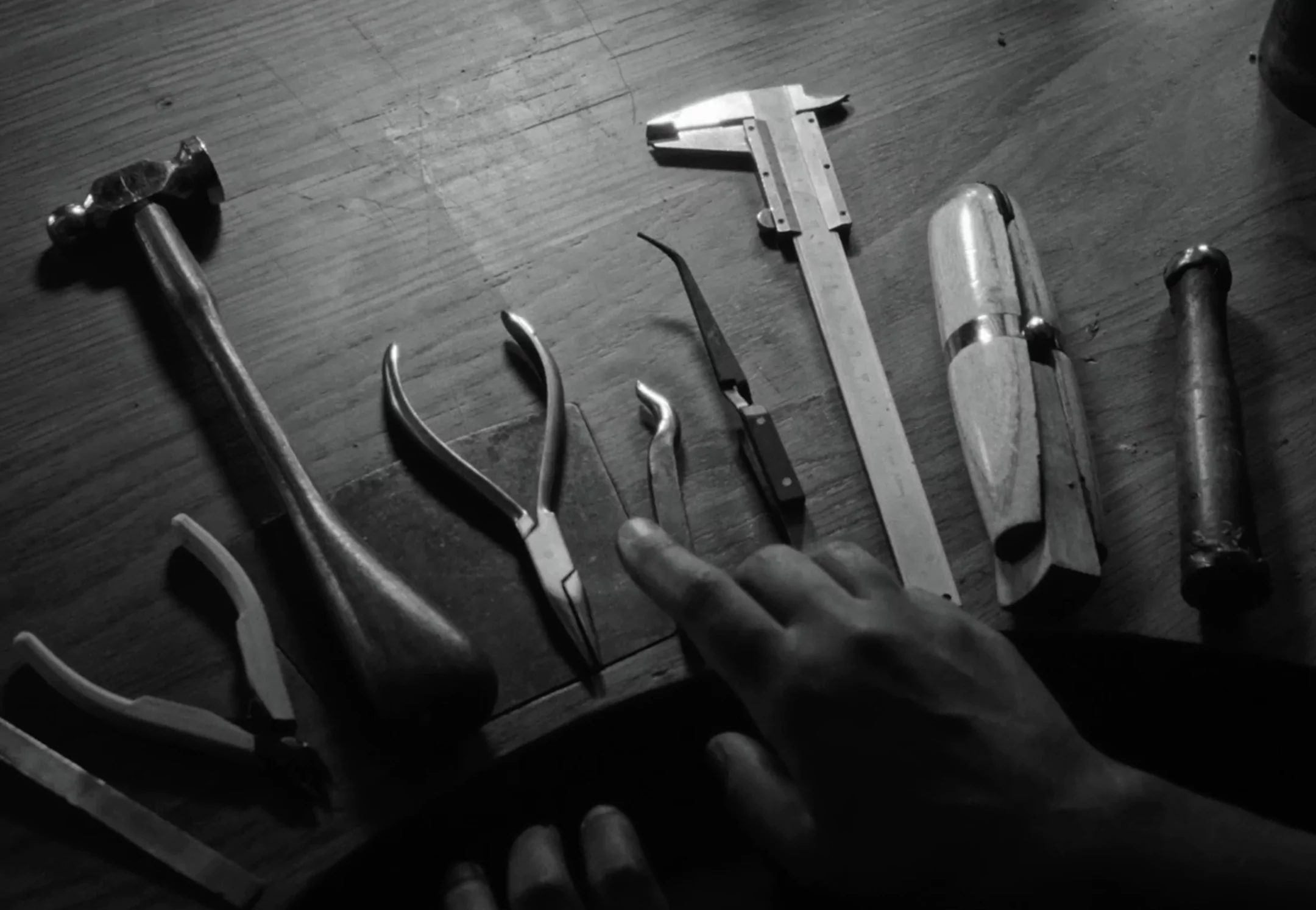 Black and white image of various hand tools on a wooden surface.