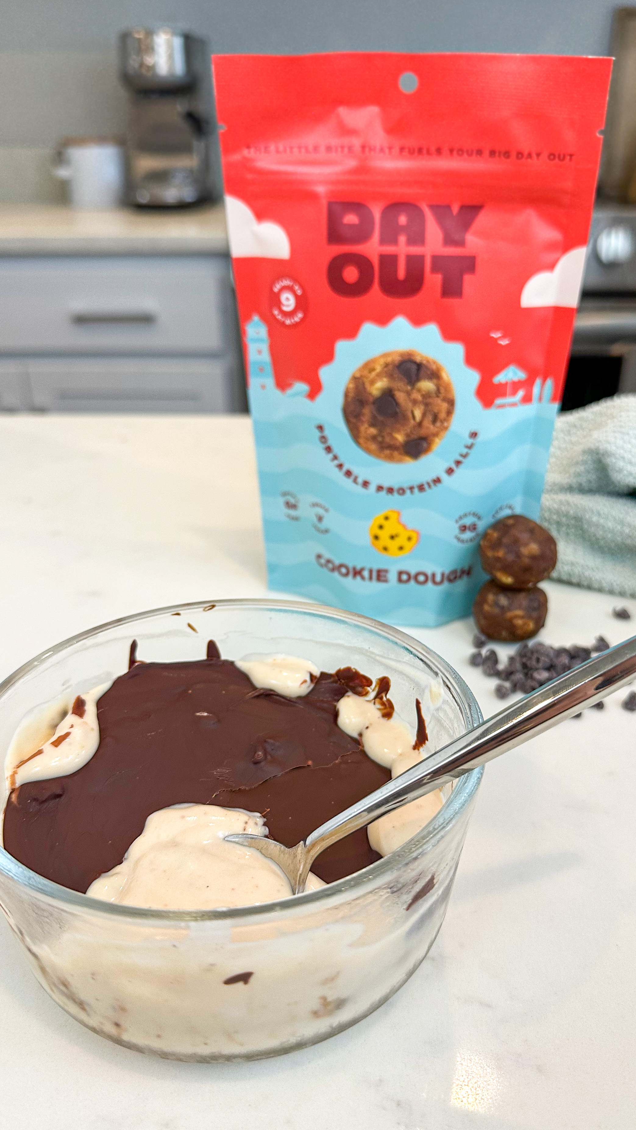 Glass bowl with chocolate and cream, protein balls, and packaging on a kitchen counter.