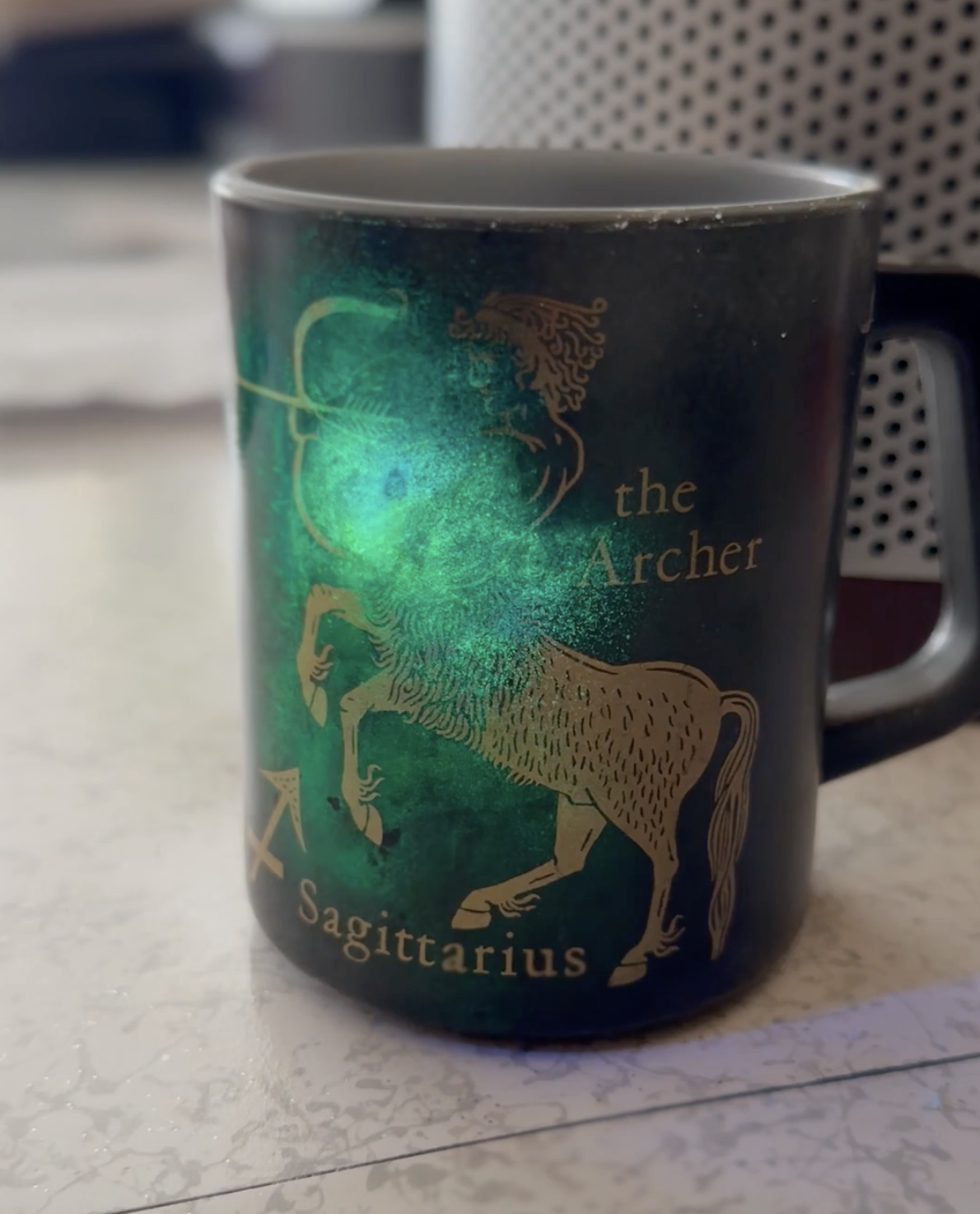 A dark mug with a gold Sagittarius design, illuminated by a bright green light from within.