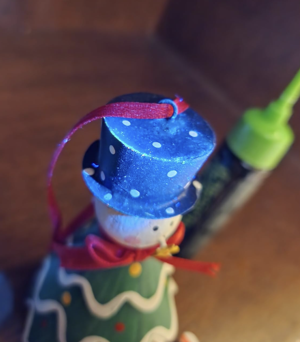 A close-up of a wooden snowman ornament with a glittery blue polka-dot top hat and red scarf.
