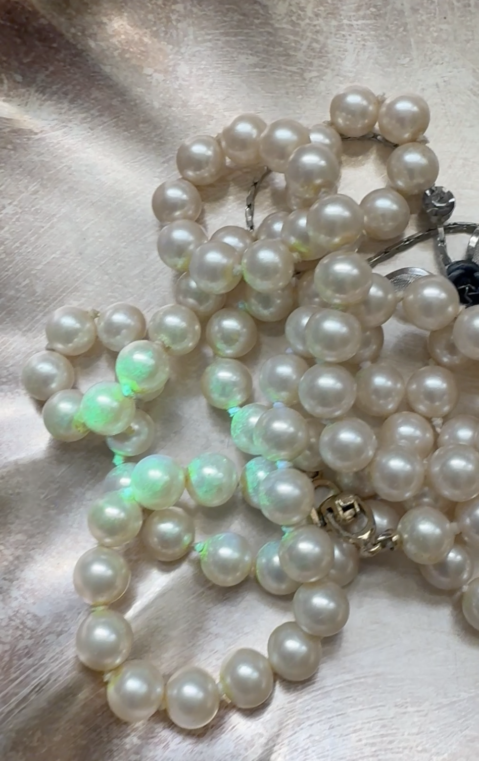 A close-up of a tangled pearl necklace, with some pearls glowing green, resting on a shimmering surface.