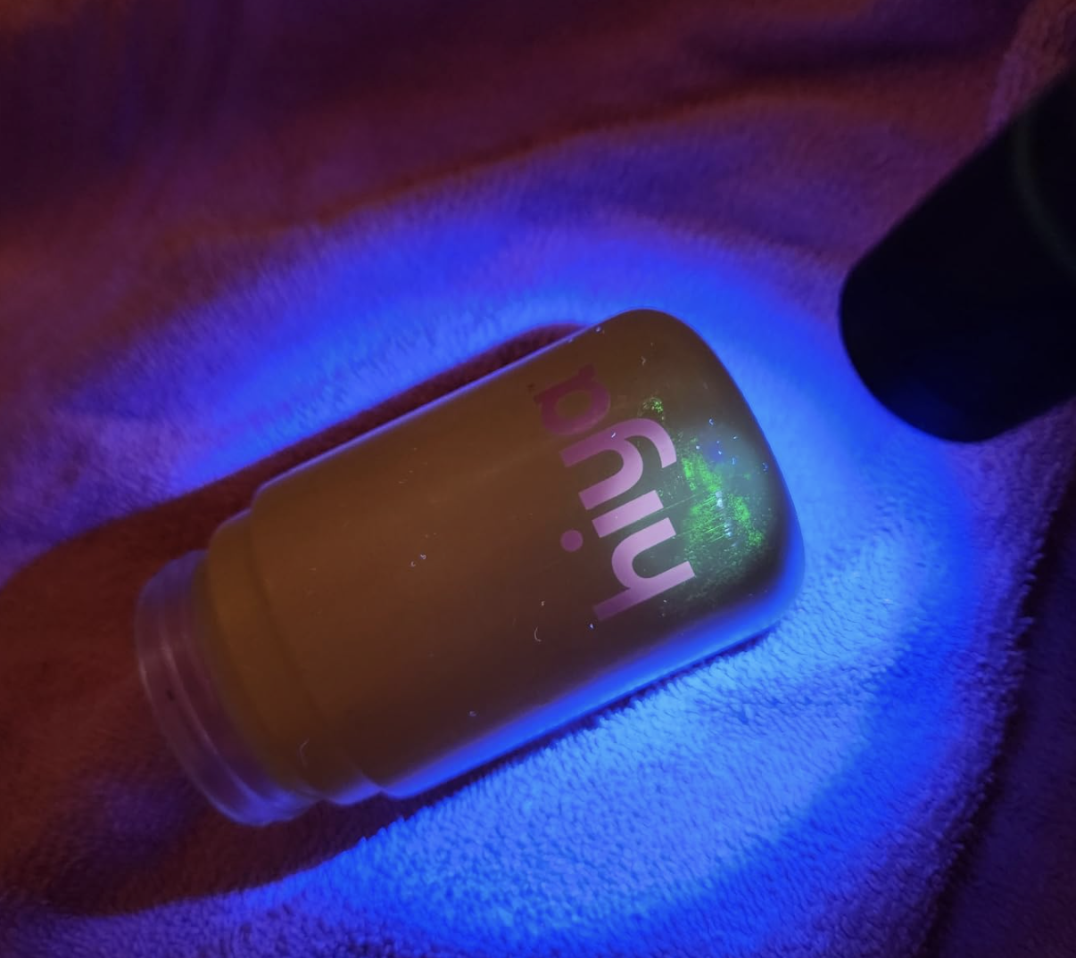A yellow bottle with the word 'hiya' on it, fluorescing green under a blue UV light.
