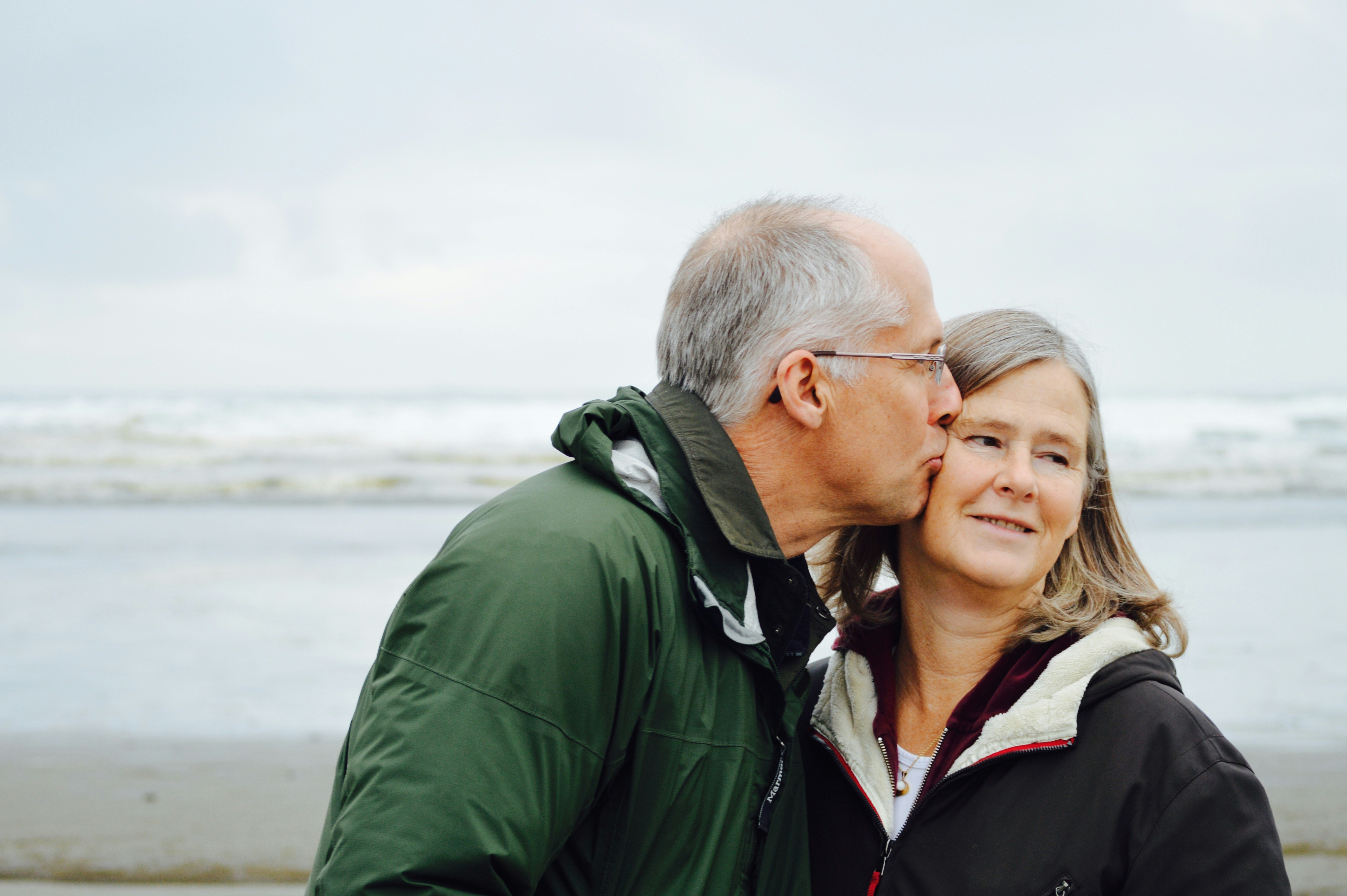 Man kisses woman on cheek at the beach.