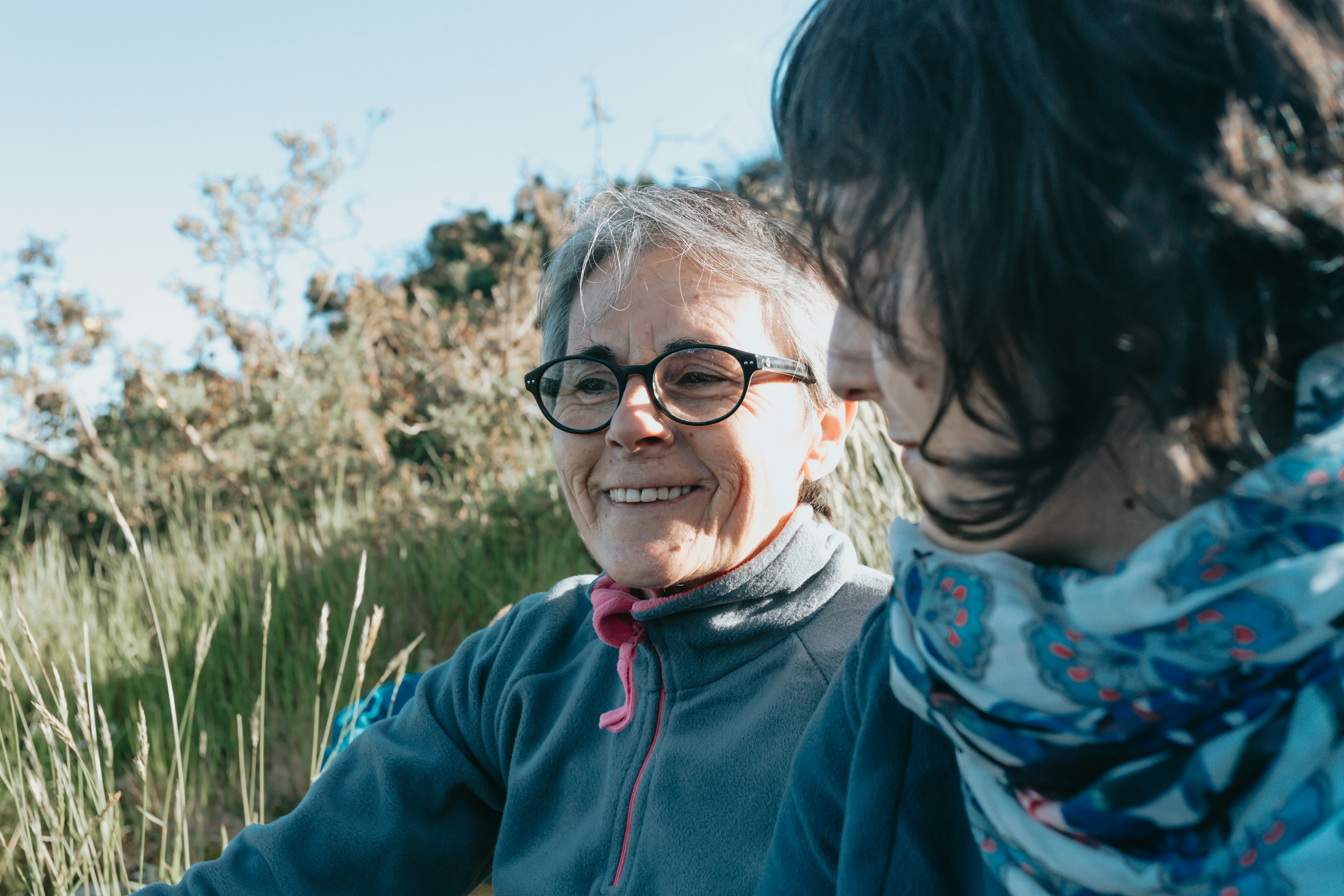 Two people smiling outdoors, surrounded by greenery.