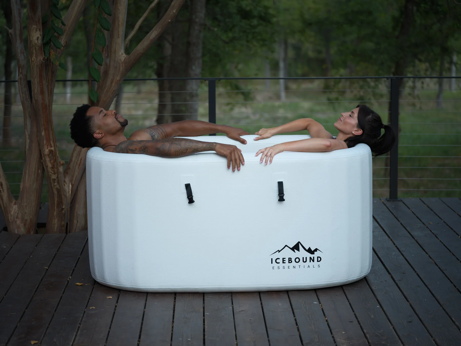 Two people relaxing in a white ice bath on a wooden deck.