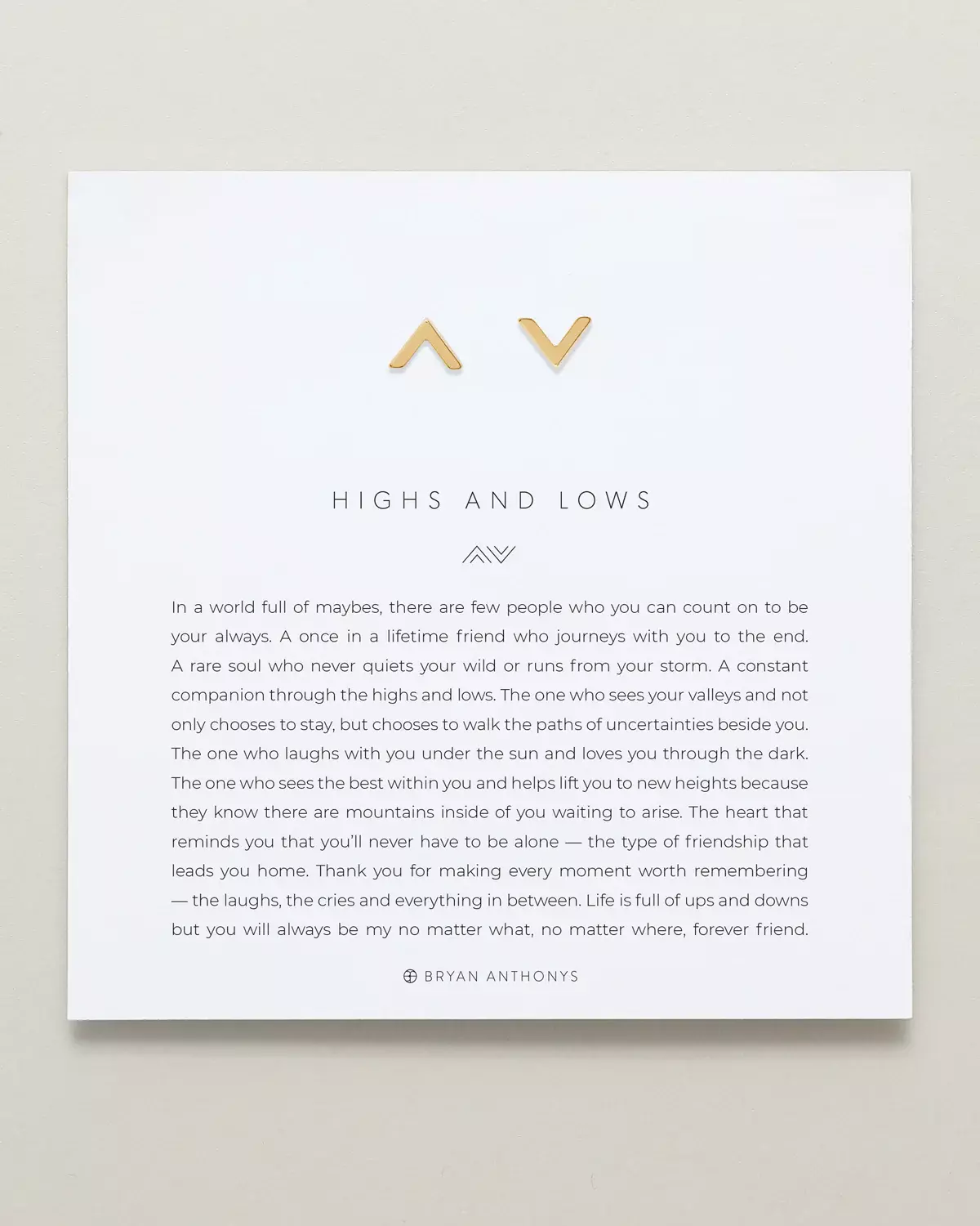 A pair of matching gold stud earrings, one shaped like an upward arrow (mountain/high) and the other like a downward arrow (valley/low), are displayed on a white card. The card features the title 'HIGHS AND LOWS'.