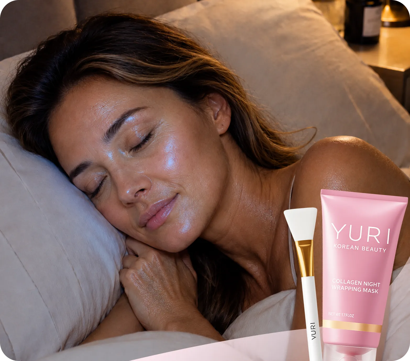 A woman with dewy skin sleeping peacefully next to a pink tube of face mask and an applicator.
