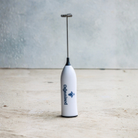 A white handheld milk frother standing upright on a wooden surface.