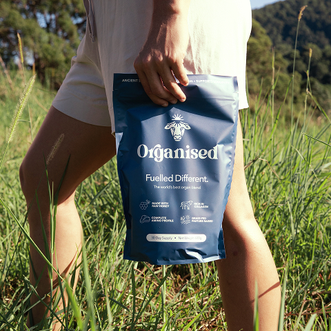 Person holding a blue bag labeled 'Organised' in a grassy field.