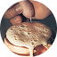 A hand holding a macaron with frothy liquid being poured on top.