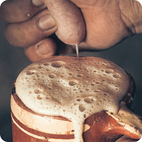 Hand pouring liquid into a frothy mug.