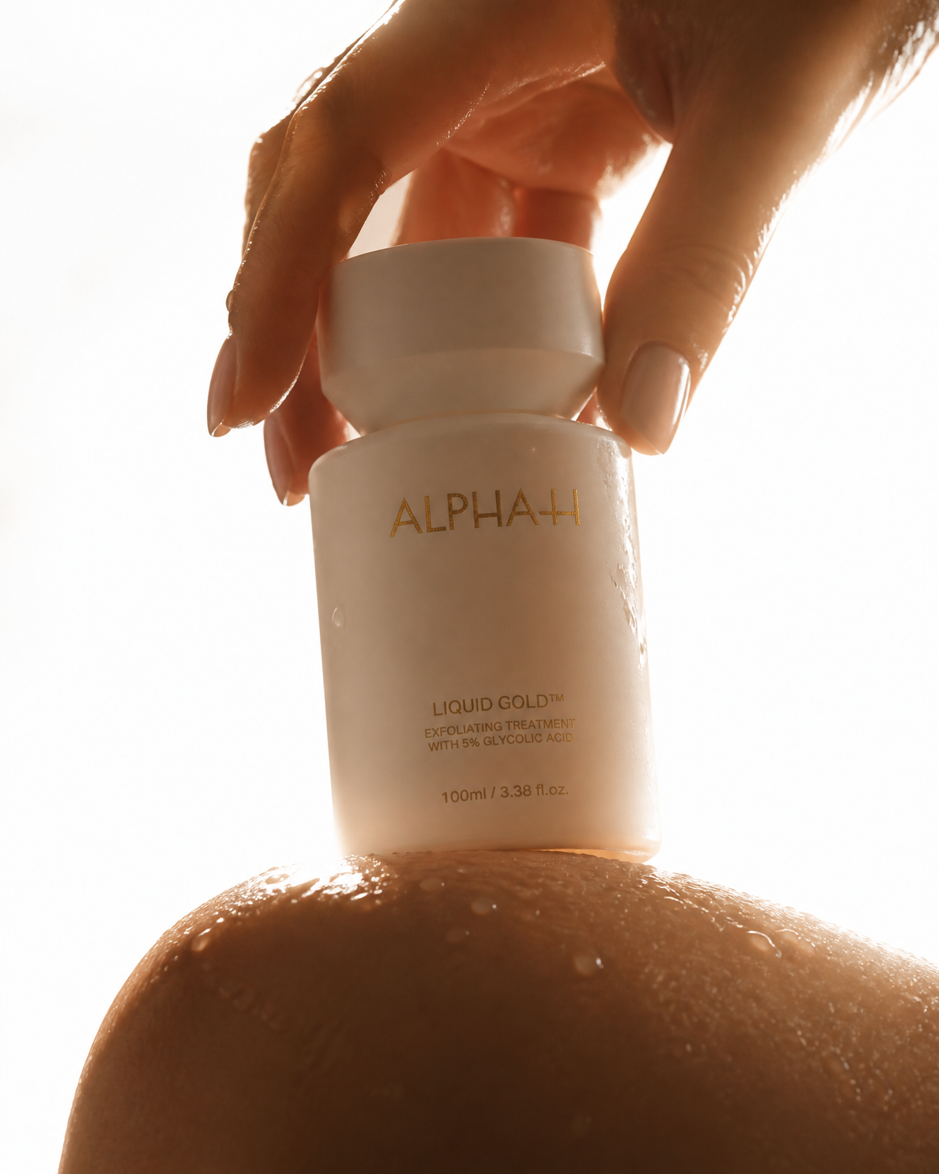 A wet hand holds a bottle of Alpha-H Liquid Gold resting on a wet shoulder.