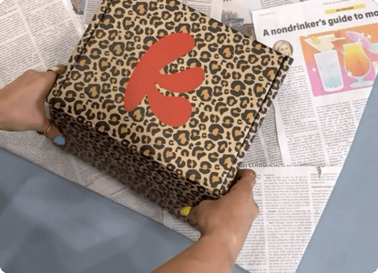 Hands holding a leopard print box with a red logo on newspaper.