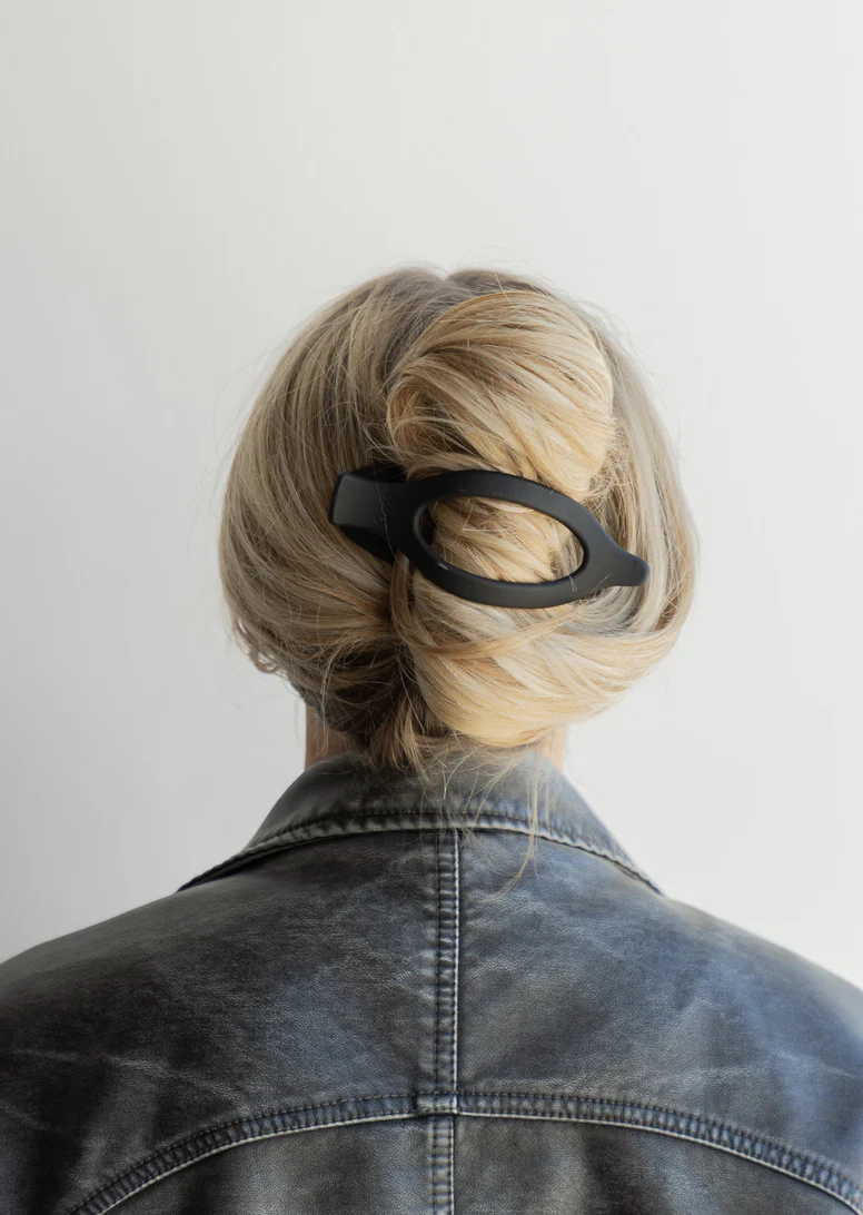 Back view of a person with blonde hair in a bun, wearing a leather jacket.