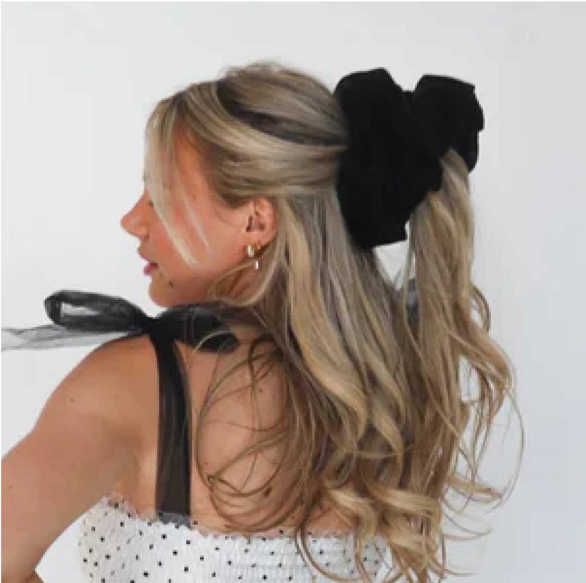 Woman with long blonde hair in a black bow, wearing a polka dot dress.