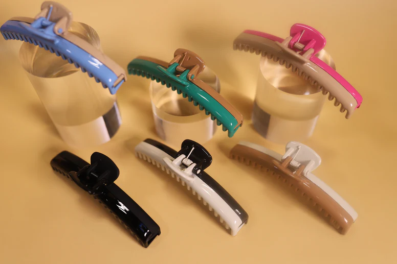 Six colorful hair clips displayed on cylindrical stands.