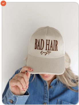Person wearing a beige cap with 'BAD HAIR' text, partially covering face.