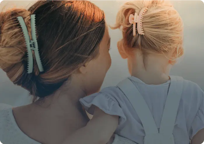 A woman holding a child, both with hair clips, viewed from behind.