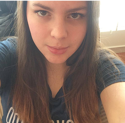 A person with long hair wearing a dark shirt, looking at the camera.