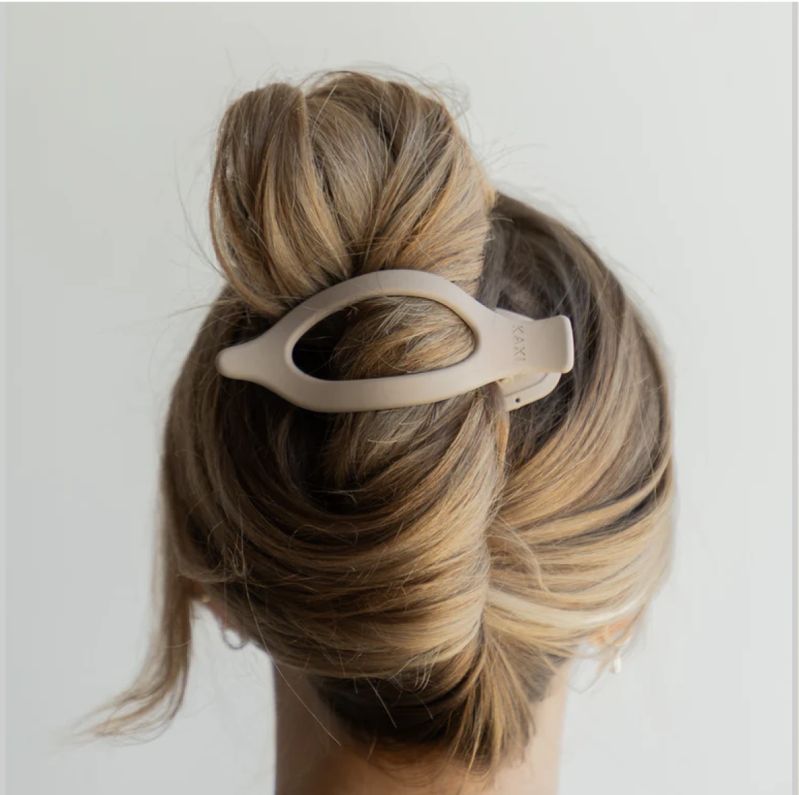 Back view of a bun hairstyle secured with a beige hair clip.