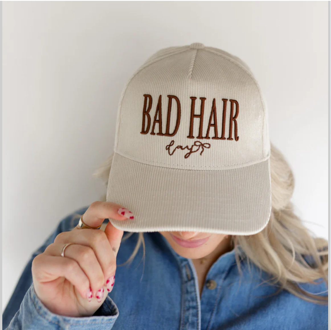 Person wearing a beige cap with 'Bad Hair Day' text.