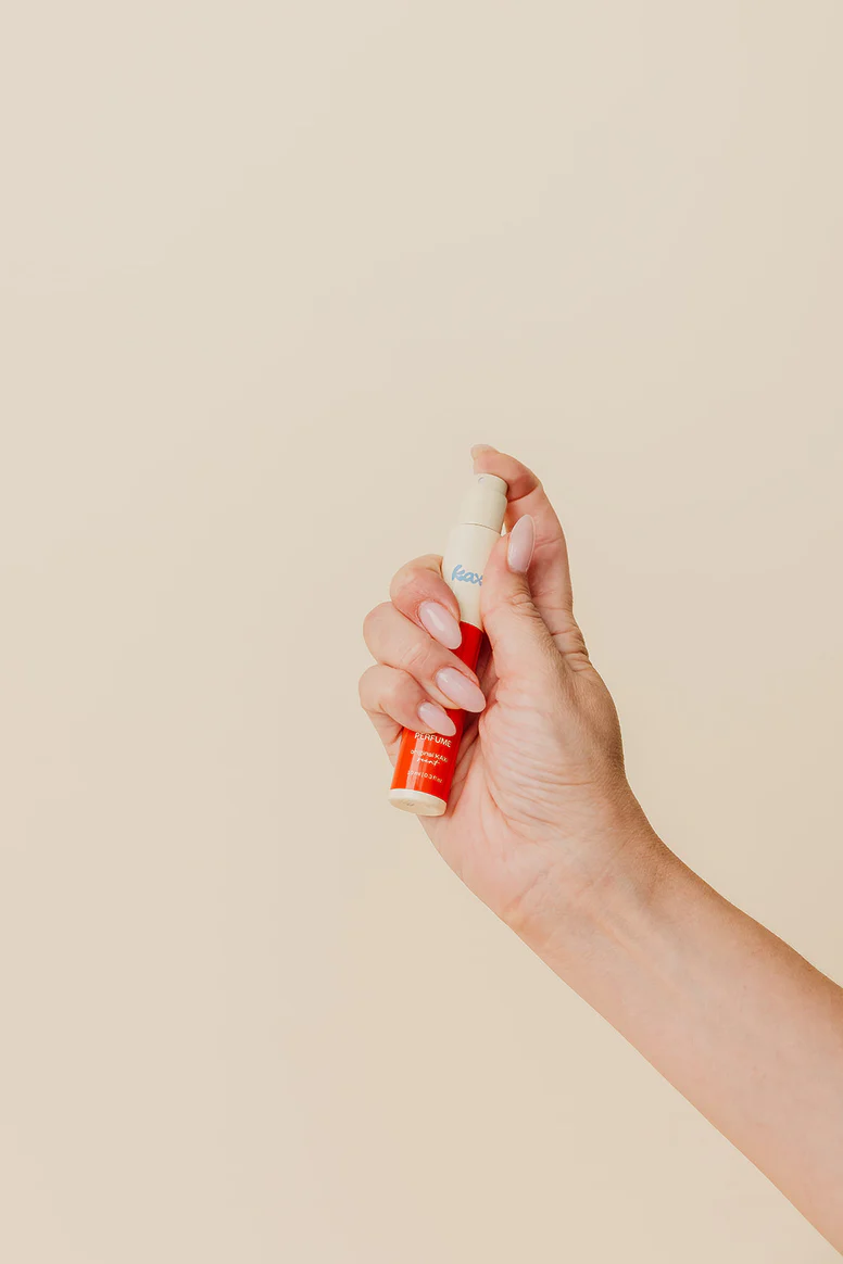 Hand holding a small spray bottle against a beige background.