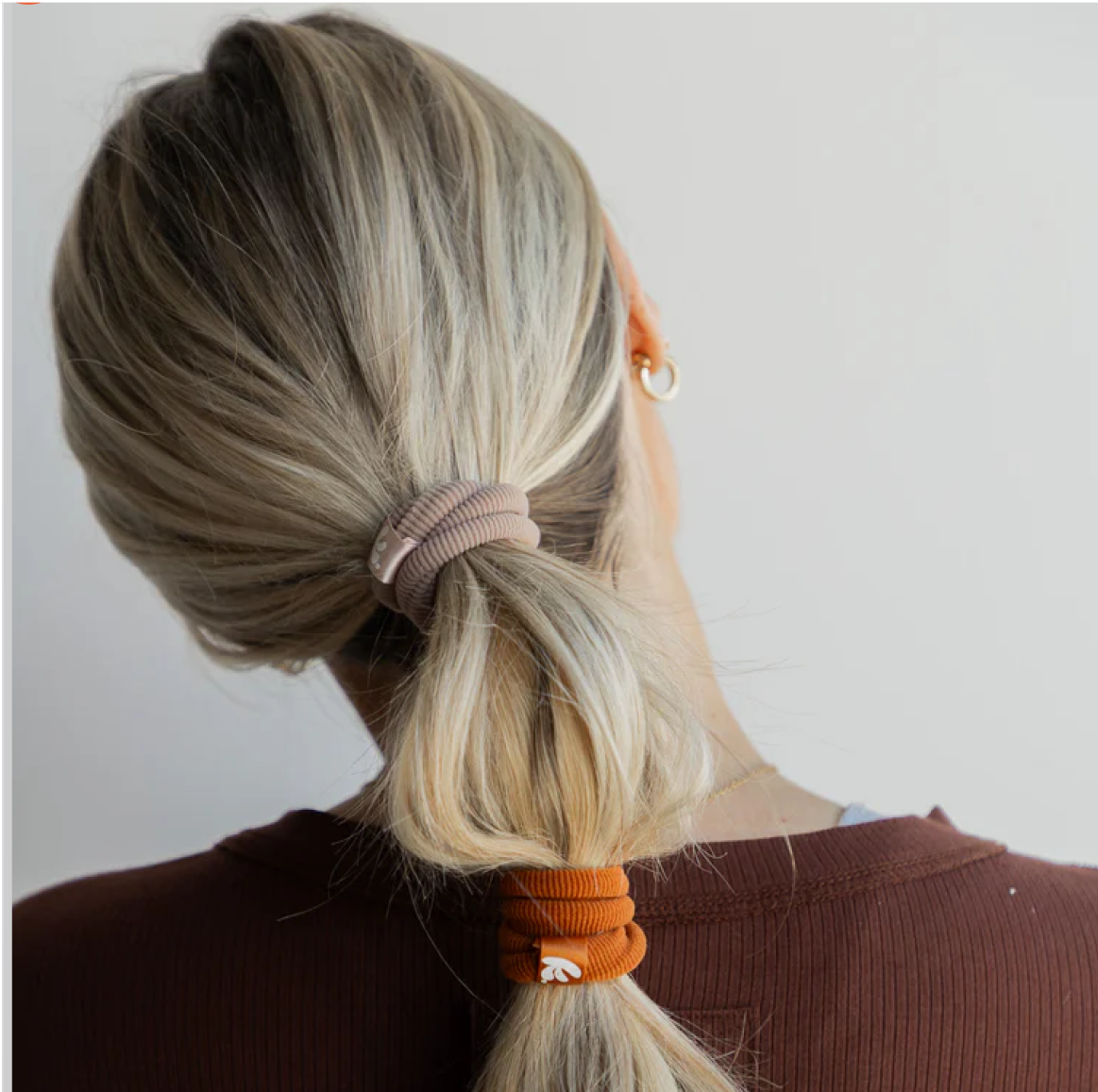 Woman with blonde hair in a ponytail, wearing brown top and gold earring.