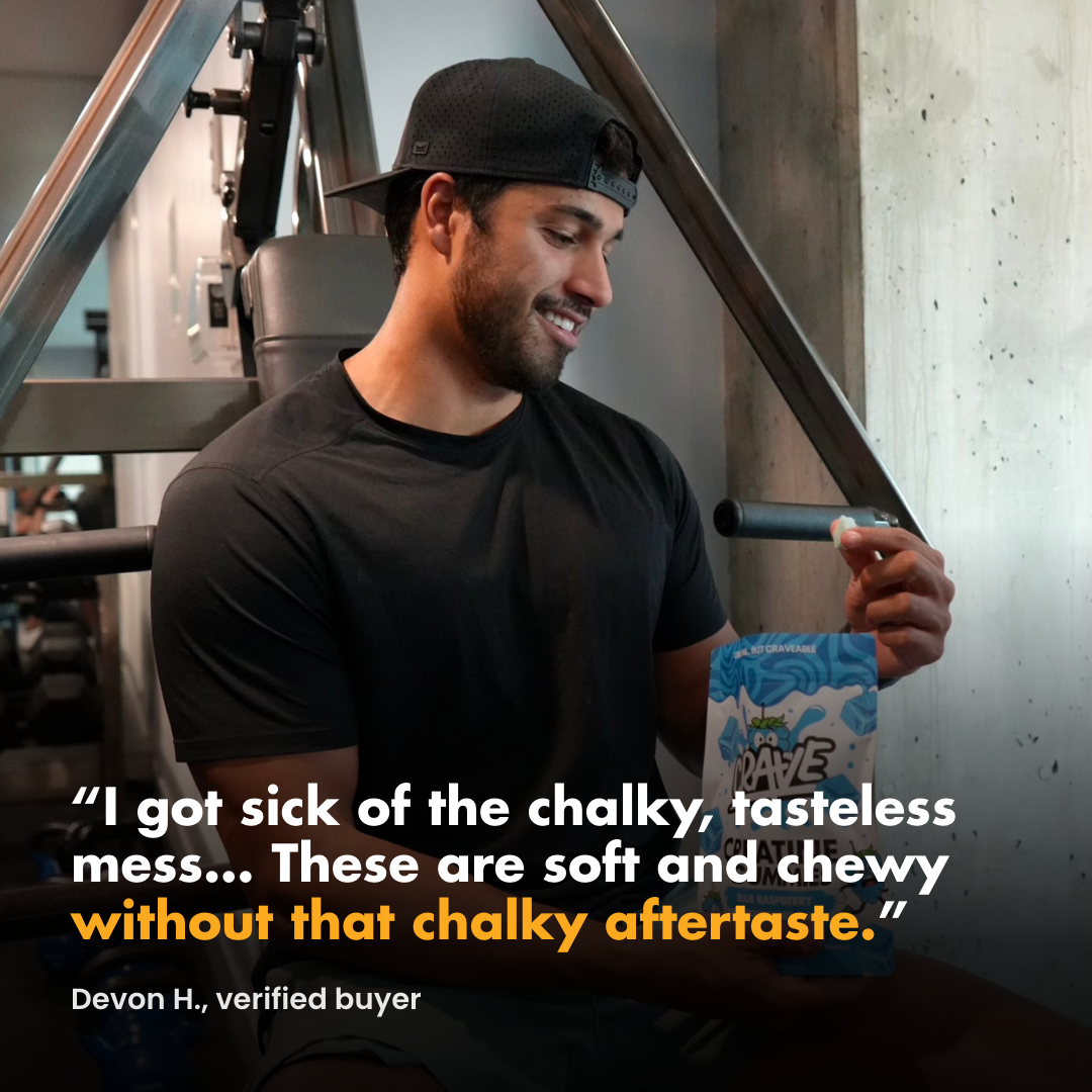 A man in a gym smiles while holding a bag of supplements and one chewable supplement.